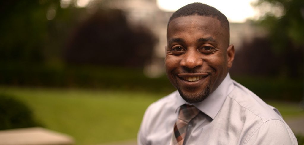 Fordham alumnus Mahlon Bailey sitting on a wall in front of Duane Library on the Rose Hill campus