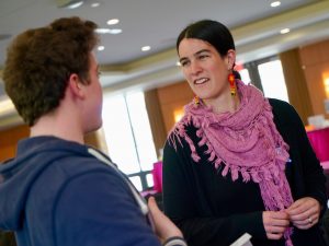 A woman wearing a pink scarf speaks with a male student.