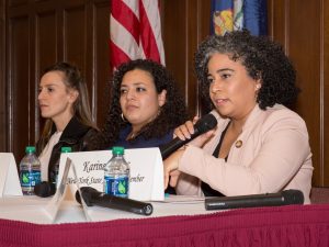 Karines Reyes holds a microphone and addresses the audience from her panel location.