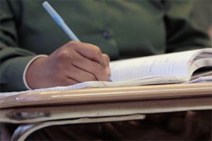 Close-up image of a notebook (and a woman's hand holding a pen) in a classroom