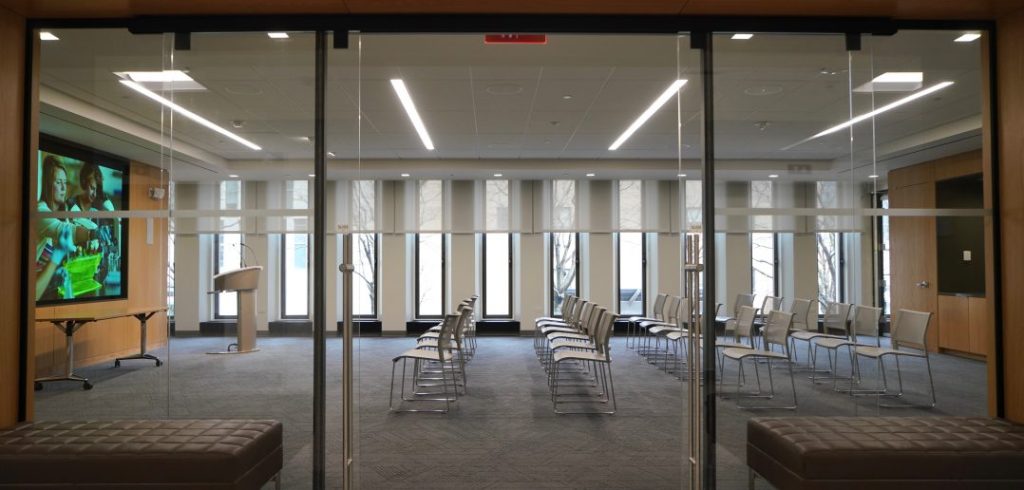 Panoramic view of the admissions office's new presentation area, featuring a wide-screen TV, four rows of chairs, and glass doors.