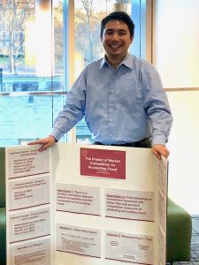 A boy stands and smiles in front of a poster board.