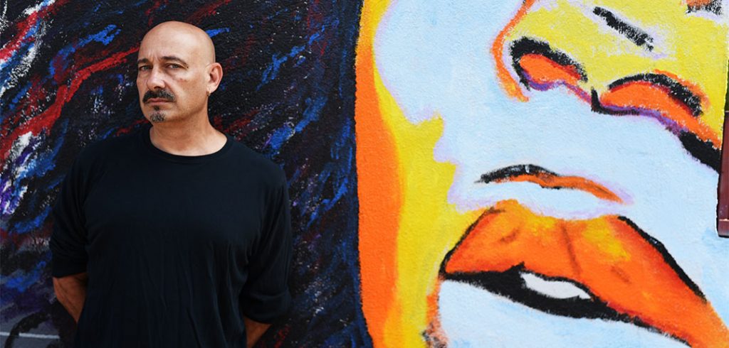 Portrait of Fordham grad Steve Romagnoli standing in front of a graffiti mural near his home in Bushwick, Brooklyn