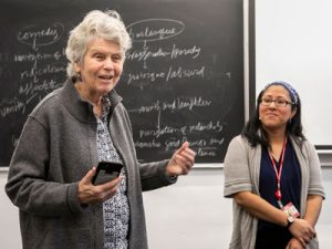 A woman with white hair speaks in front of a chalkboard