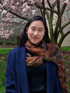 An Asian woman wearing a blue blazer and standing in front of a cherry blossom tree