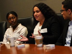 A young woman wearing a blazer speaks and gestures with her hands.