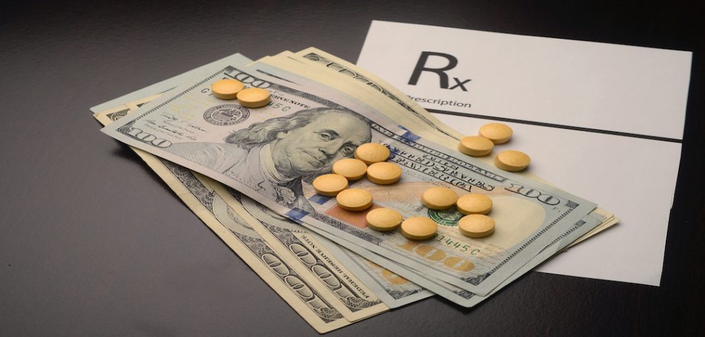 Pills are displayed on top of dollar bills to represent the costs of prescription drugs.