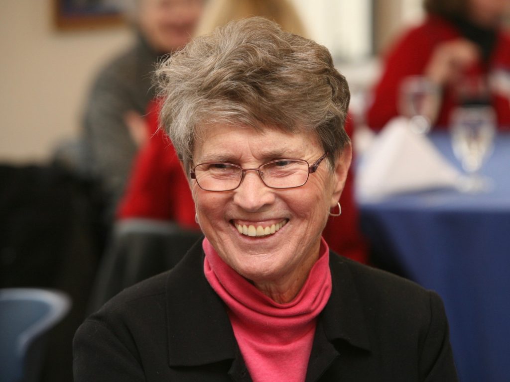 A woman in a pink turtleneck smiles.