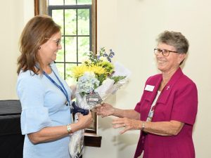 A woman in a pink shirt receives a bouquet of flowers from another woman.