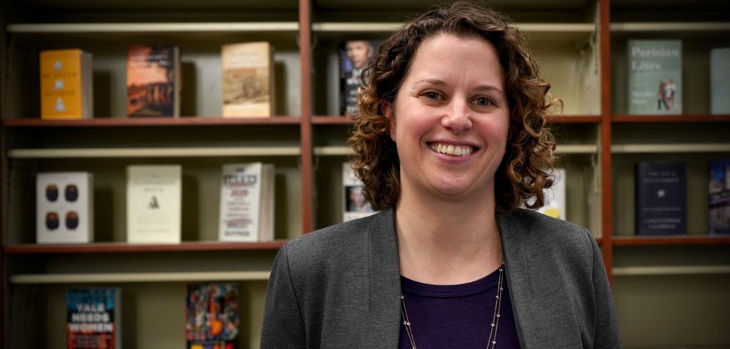 A woman smiling in front of a shelf filled with books