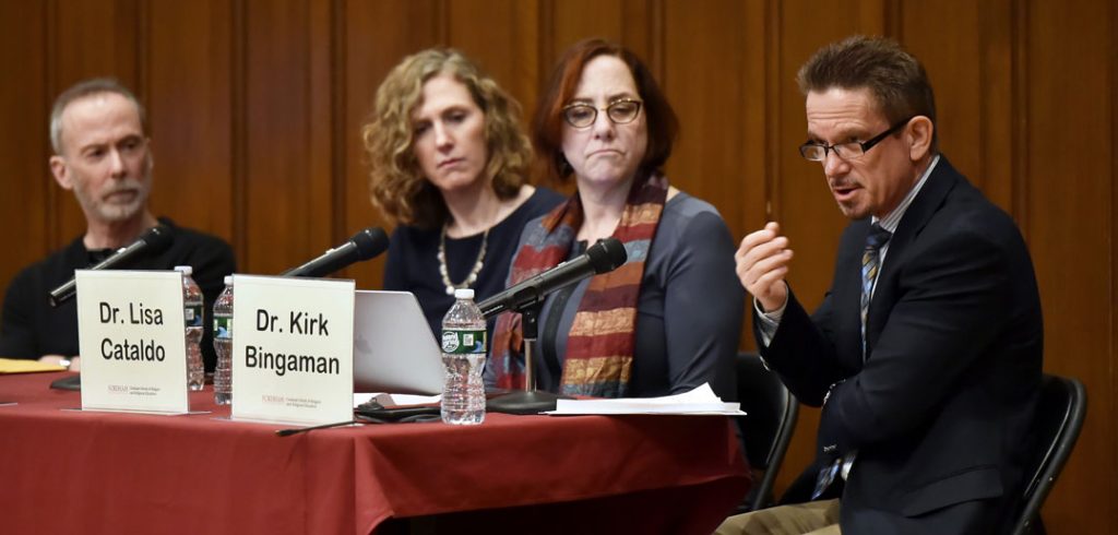 A man wearing glasses speaks next to three other people.