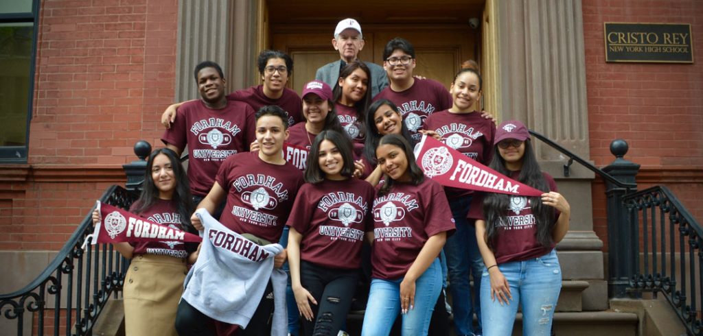 A group of teenagers wearing Fordham gear on the steps of Cristo Rey New York High School