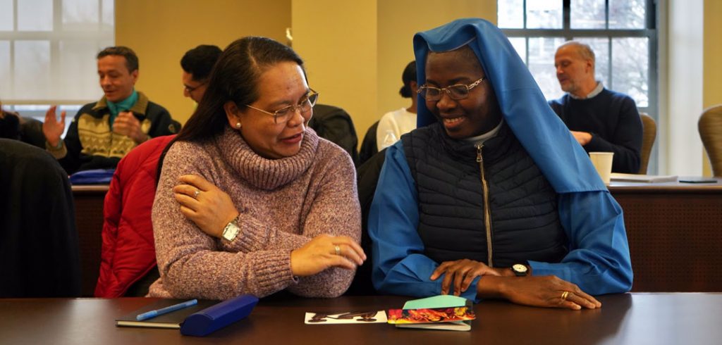 Two women sit beside each other and smile at cards on a table before them.