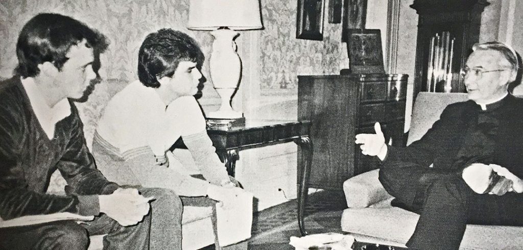 A black-and-white 1984 photo shows two Fordham student journalists, John Breunig and Dan Vincelette, interviewing Joseph A. O'Hare, S.J., then the new president of Fordham, in the president's office at Rose Hill.