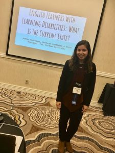 A woman stands in front of a PowerPoint presentation.