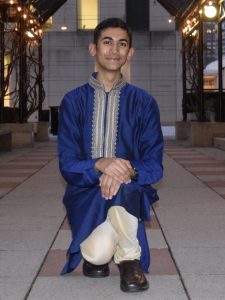 A young man wearing an Indian outfit and kneeling on the floor