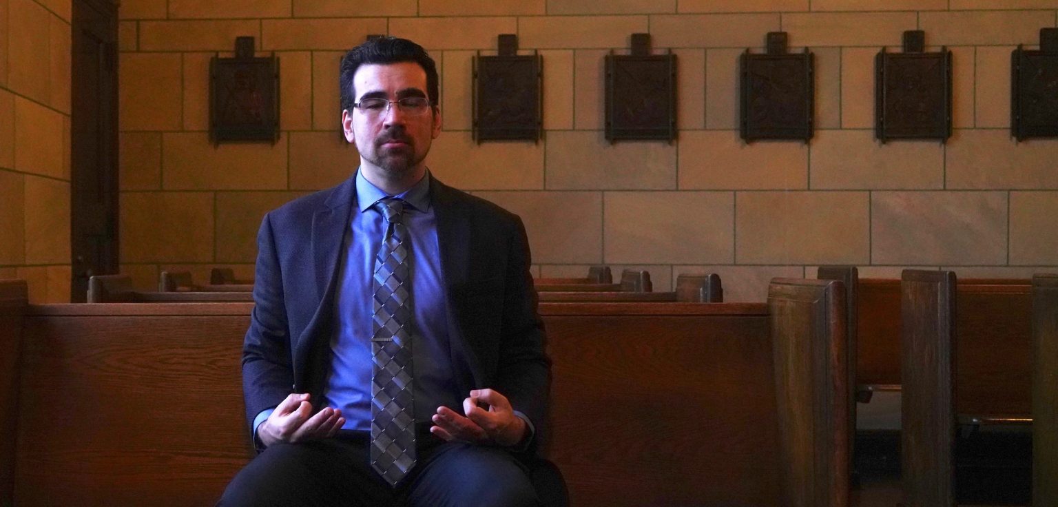 A man sitting on a wooden church pew with his eyes closed