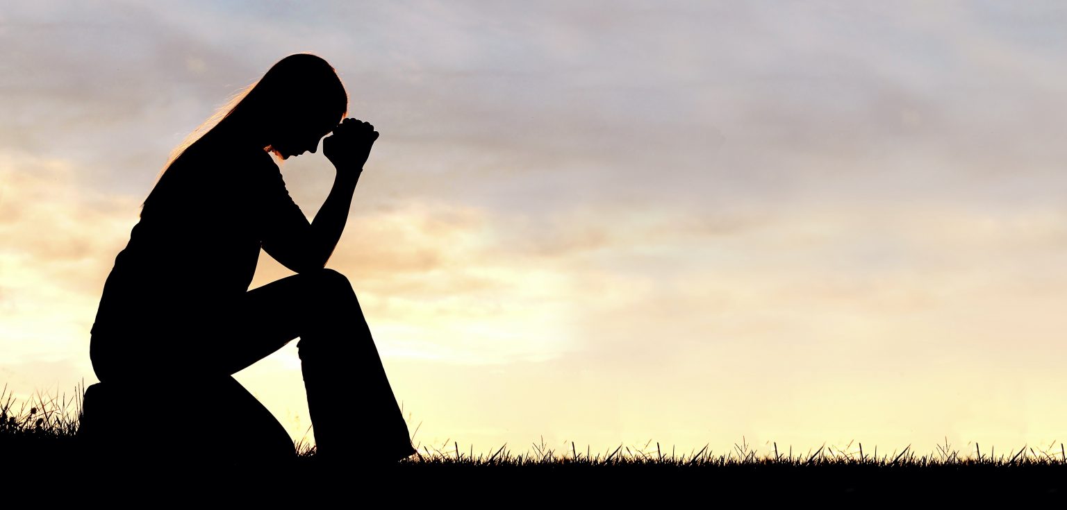 Silhouette of a woman sitting with her elbow propped against her knee outside