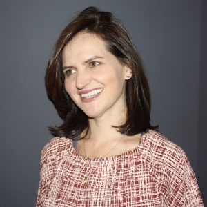 A woman wearing a red and white criss-cross pattern dress smiles and looks off camera.