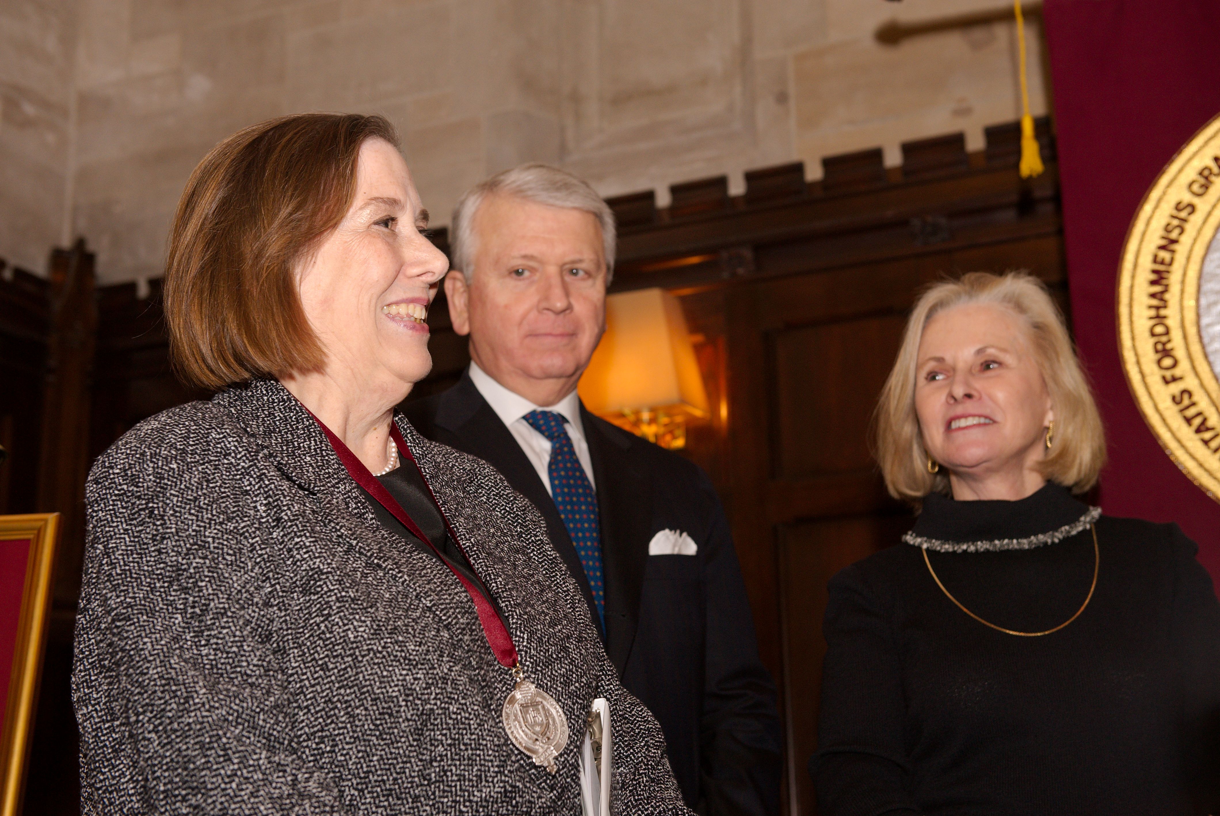 A woman stands and smiles with a medal around her neck, besides a man and another woman.