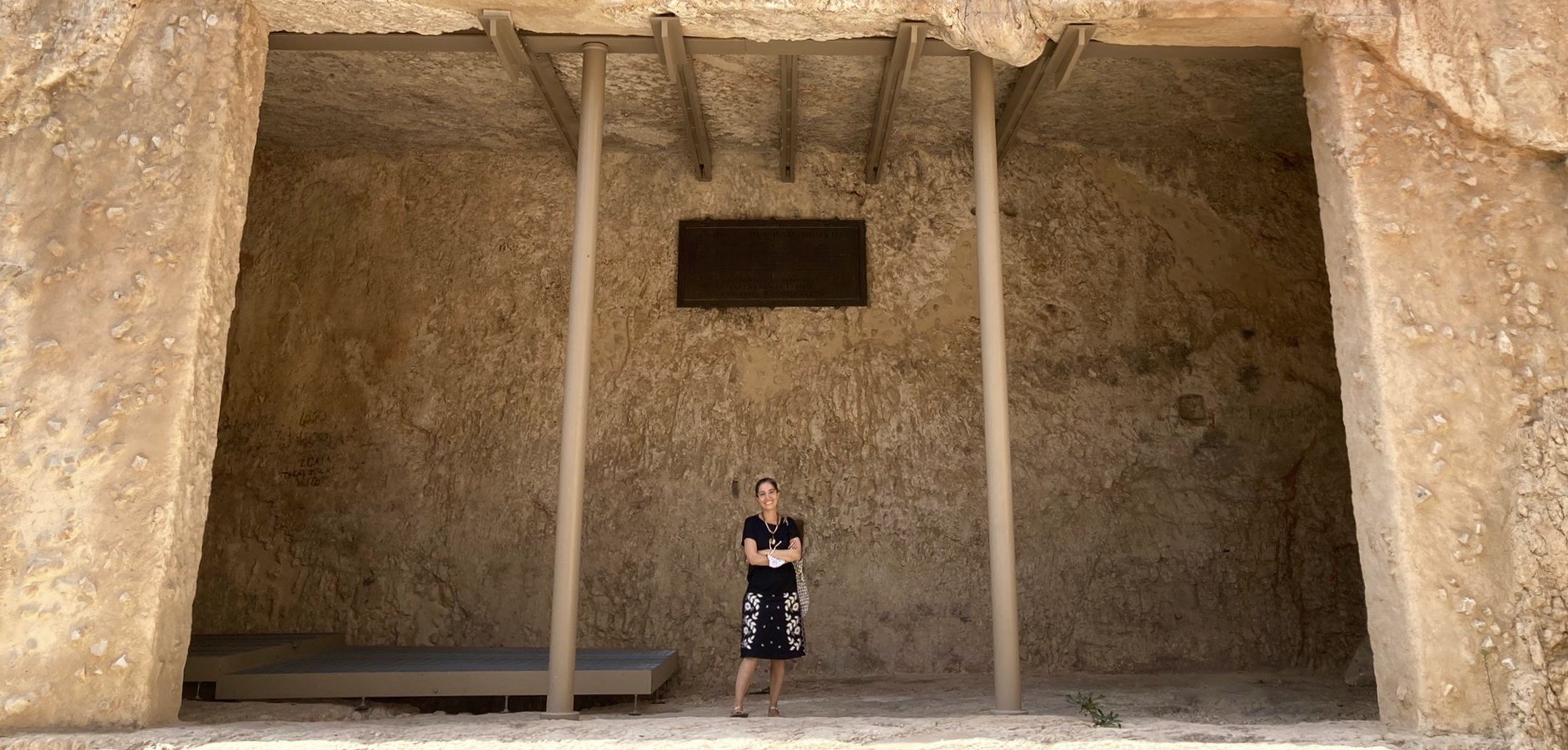 A tiny woman stands and smiles in a huge, cavernous room.