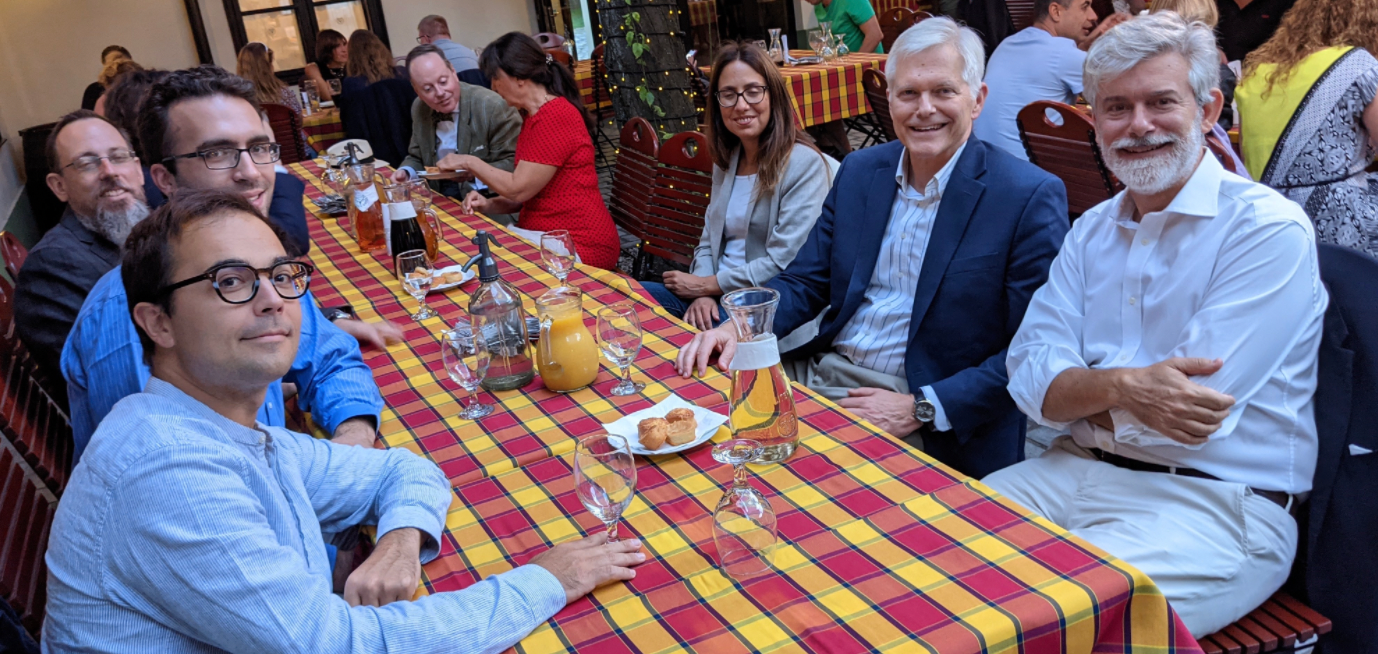 A group of people sit at a picnic table and smile.