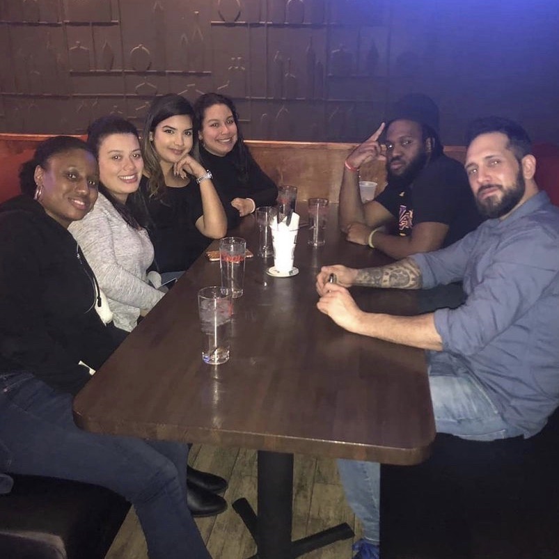 Six people seated around a wooden table smile.