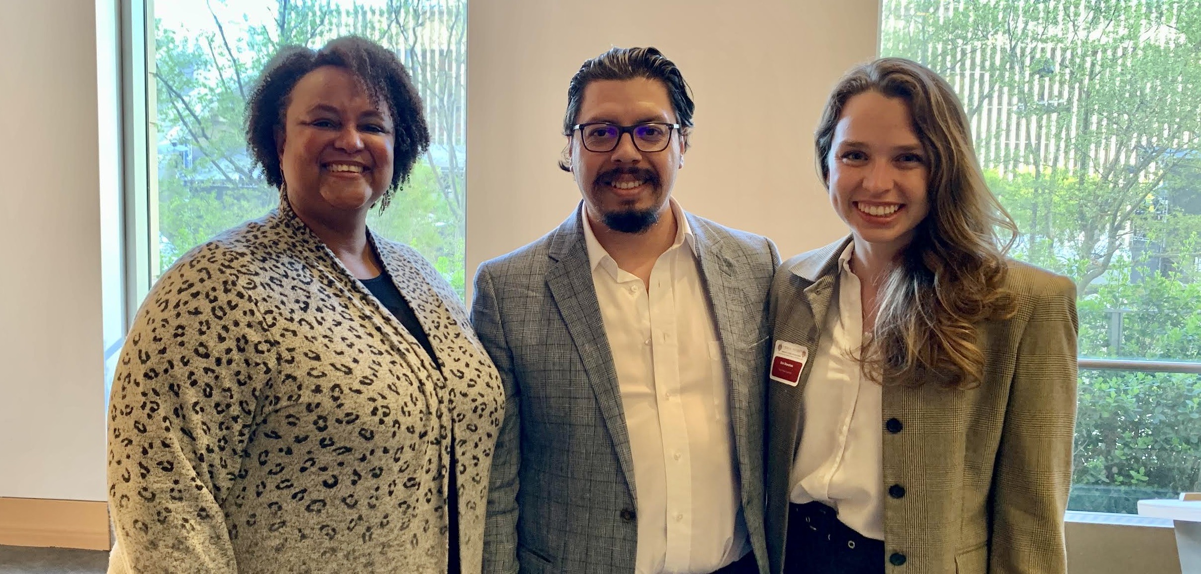 Three people wearing professional outfits smile.