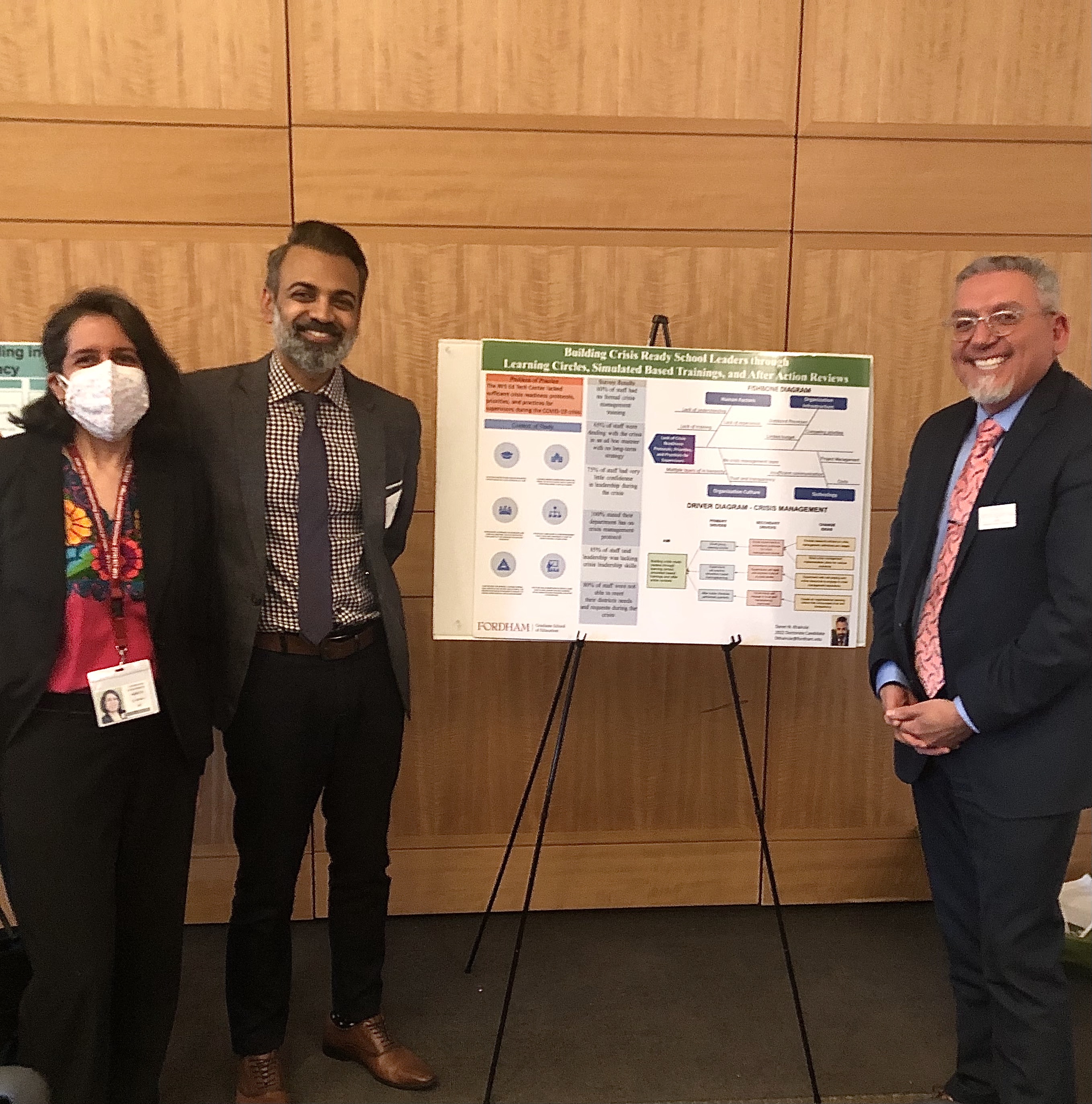 Three people stand and smile in front of a research poster.