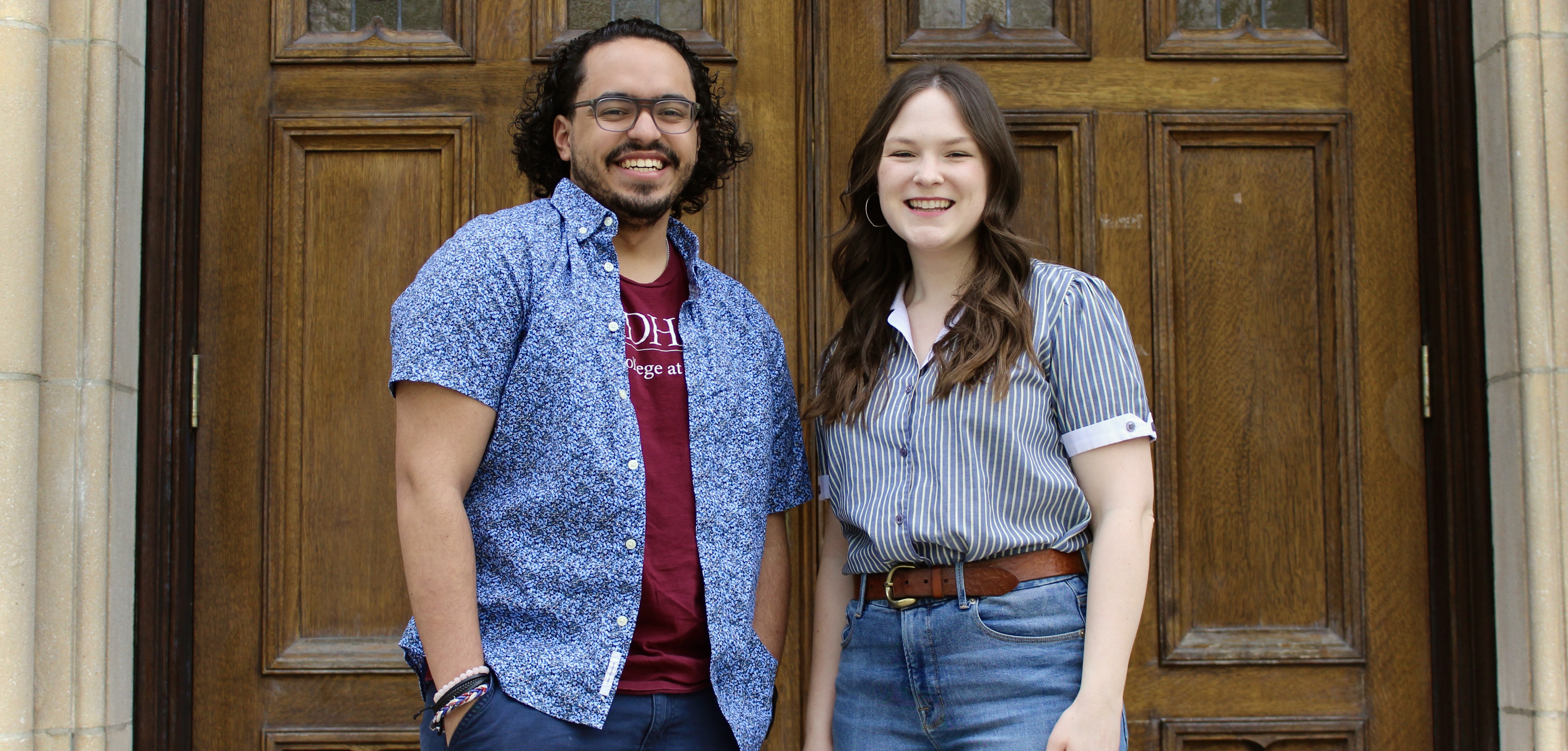 A man and woman smile in front of a set of wooden doors.