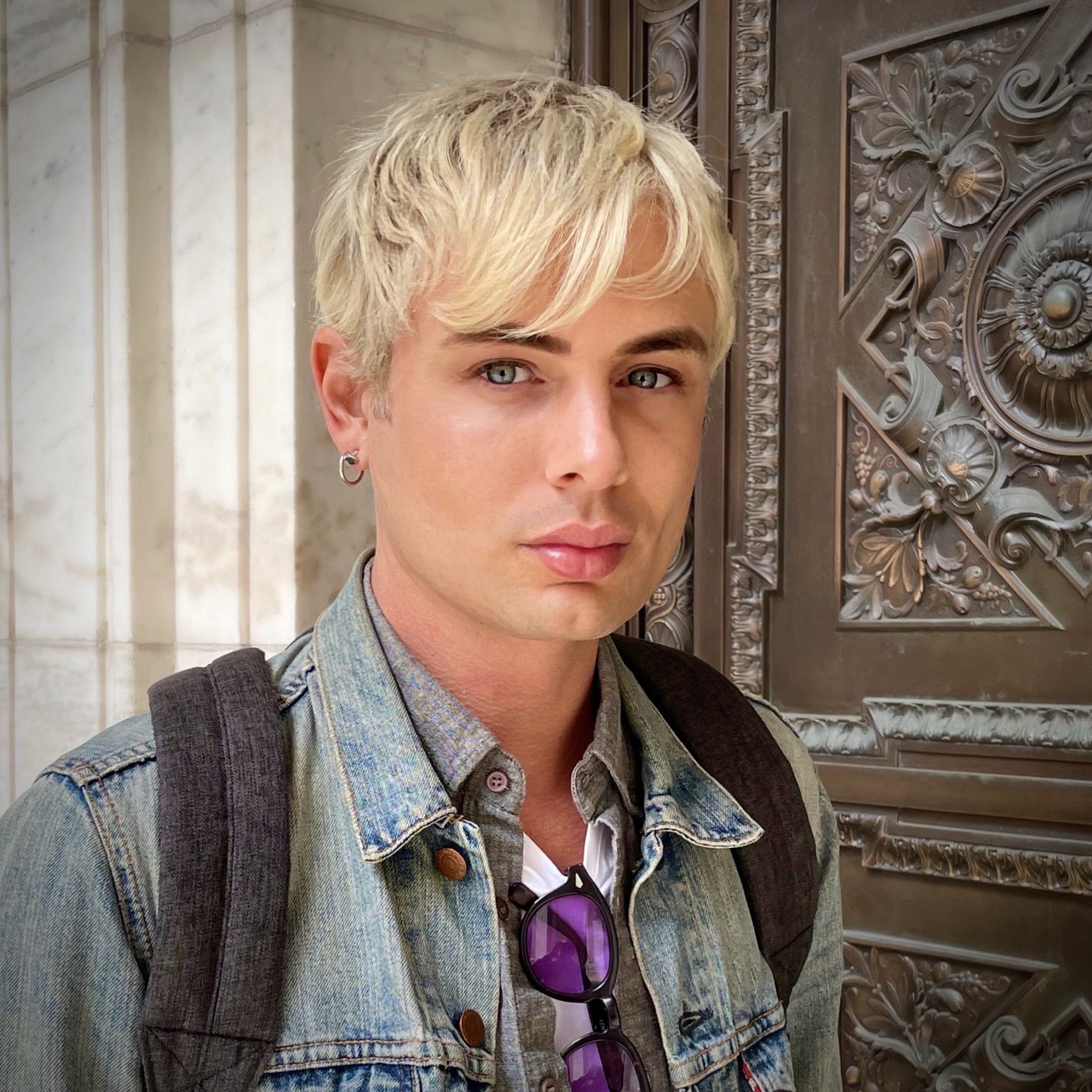 A man with blonde hair and a jean jacket smiles with his mouth closed.