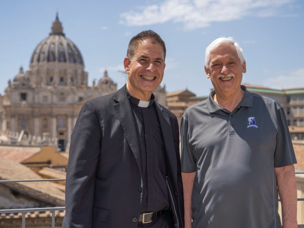 Two men smile in front of a large dome.