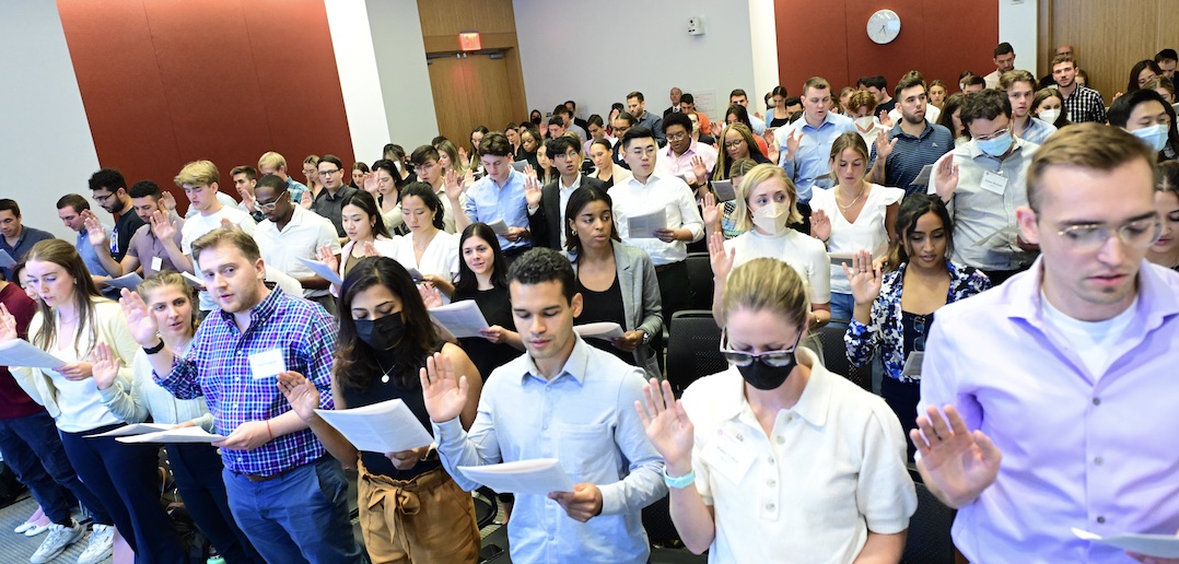 A group of standing people raise their right hand and read from a booklet.