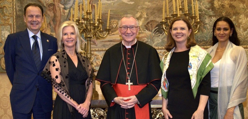 Five people stand together and smile in front of two ornate candles.