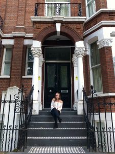 A woman sits on the steps to an apartment and smiles.