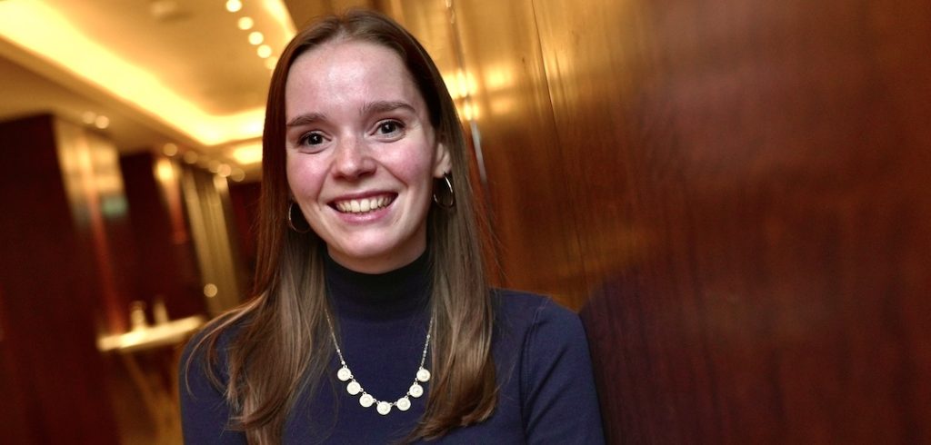 A woman wearing a necklace and a navy blue shirt smiles at the camera.