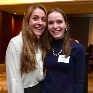 Two women wearing business attire smile at the camera.