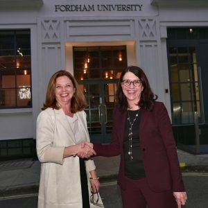 Two women in business attire shake hands in front of a building.