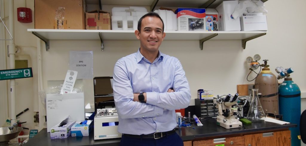 A man crosses his arms and smiles in a lab.