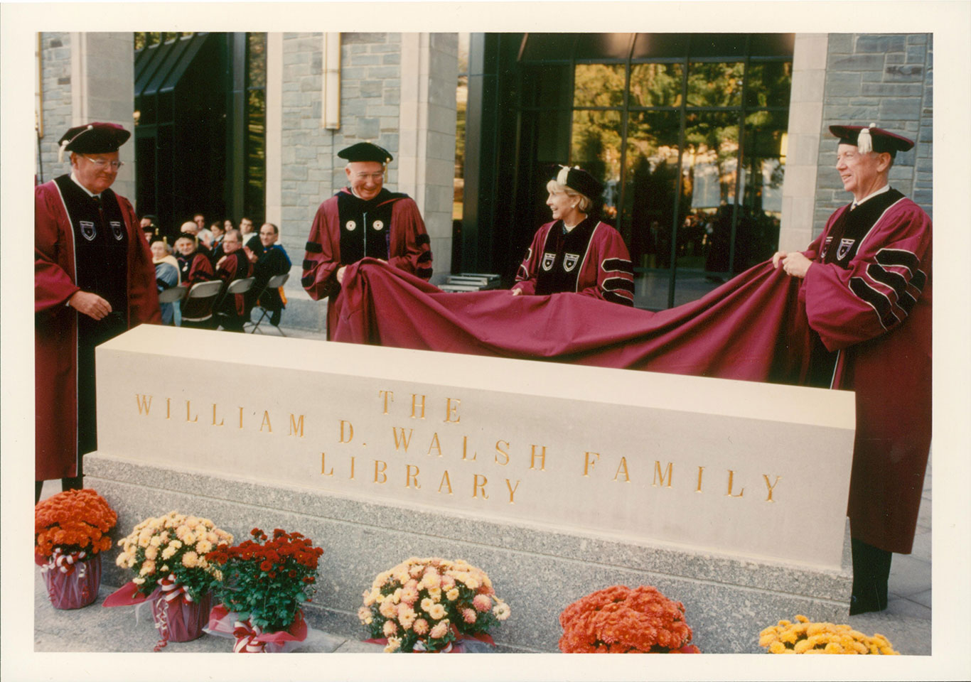 Four members of the Fordham administration remove a red cover of a sign for the Walsh Family Library