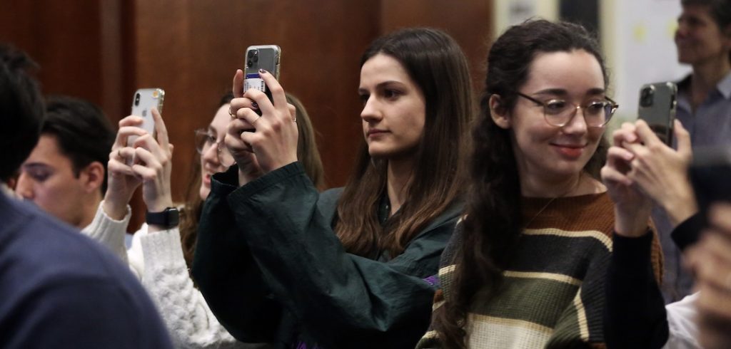 Two girls point their smartphones at something.