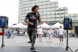 Andrew Harris dances on a stage with speakers on either side of him, and tents behind him.