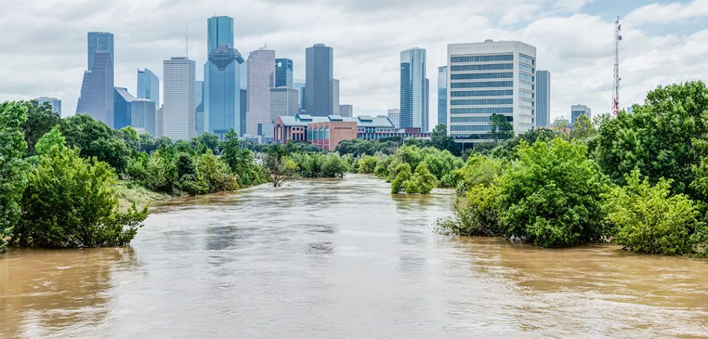 High and fast water rising in Bayou River with downtown Houston in background under cloud blue sky. Heavy rains from Harvey Tropical Hurricane storm caused many flooded areas in greater Houston area.