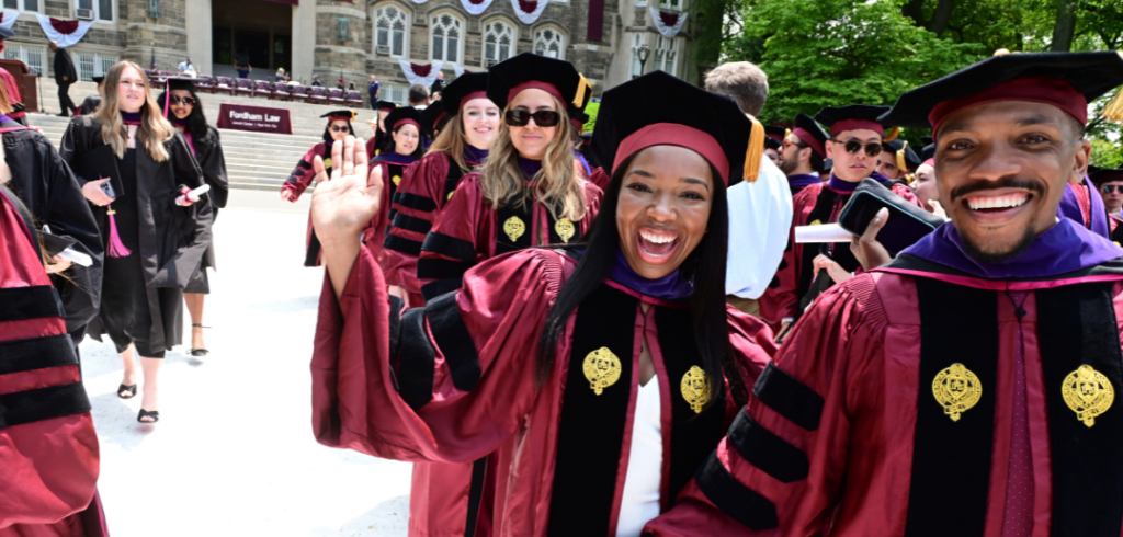 Ronald Britt ’23 and Tanecia Vasquez ’23 walking with classmates behind them. All dressed in academic robes and caps.