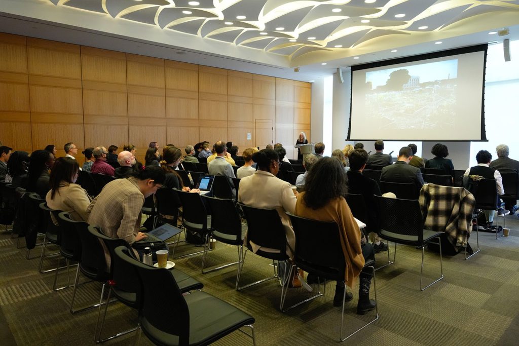 40 or so people seated in a conference room, facing a speaker at a podium.