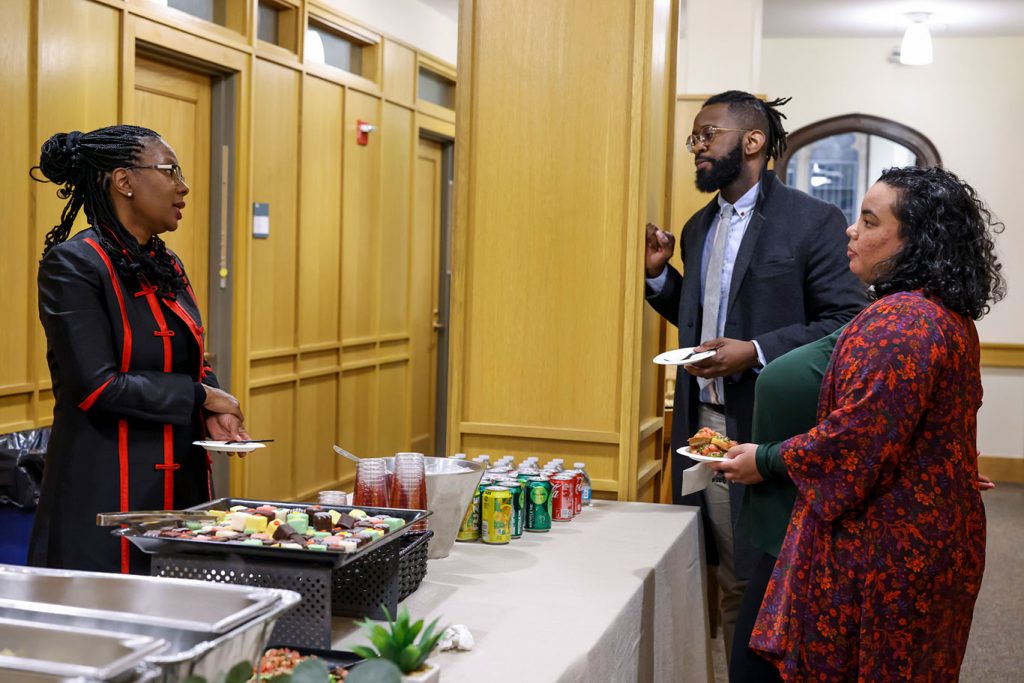 Melanie Harris standing at a table talking to an man and woman Ph.D. candidates