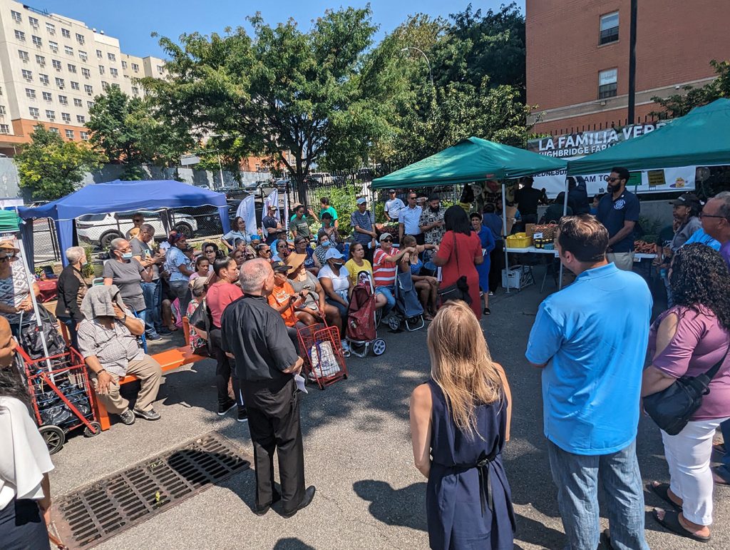 A group of people stand and sit listening to the Bronx Borough President talk