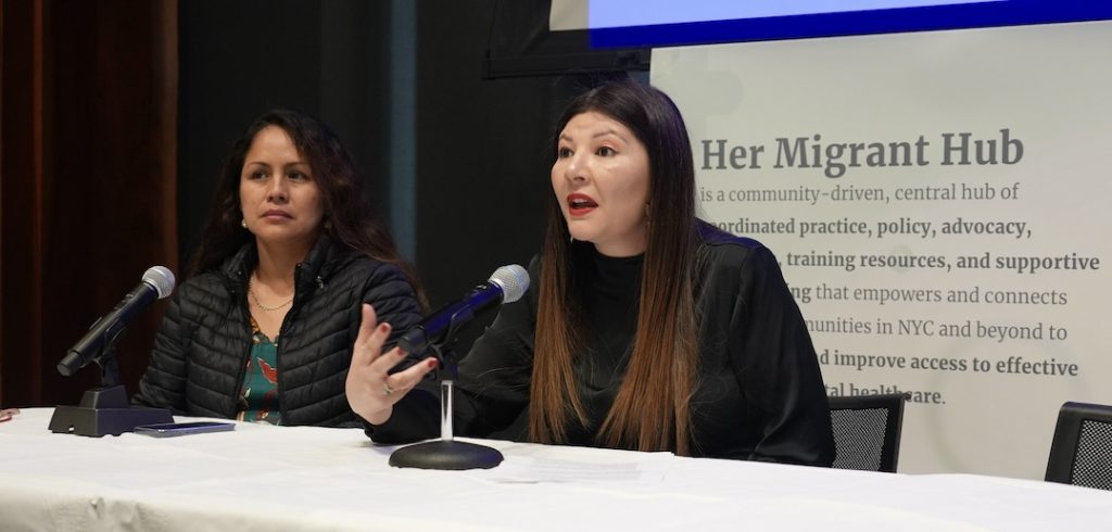 A student and a woman asylum seeker sit at a table and speak to an audience.