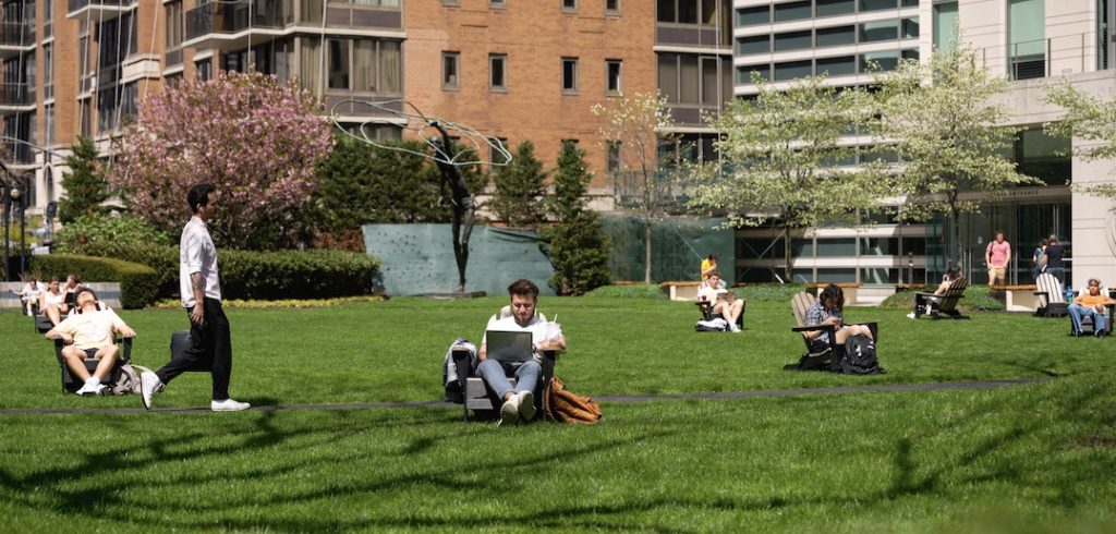 Students study in chairs and walk around the grassy plaza at the Lincoln Center campus.