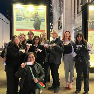 Students and faculty smile in front of the Metropolitan Opera while holding opera tickets.